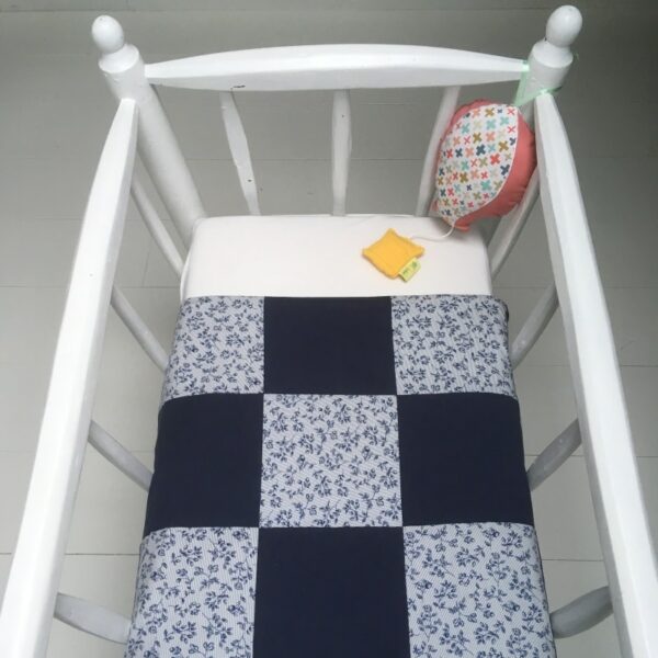 Couverture de naissance à carreaux bleus et fleuris bordée dans un berceau